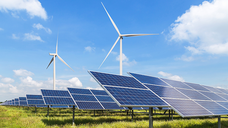 Windränder und Photovoltaikpanele auf grüner Wiese, blauer Himmel im Hintergrund